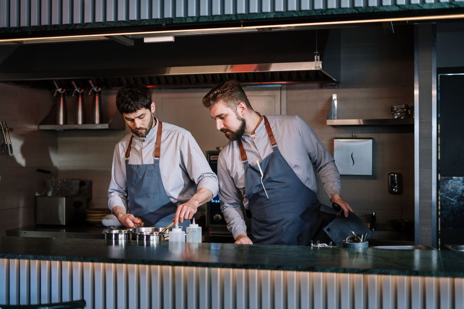 Deux cuisiniers coordonnent la préparation des plats derrière le passe